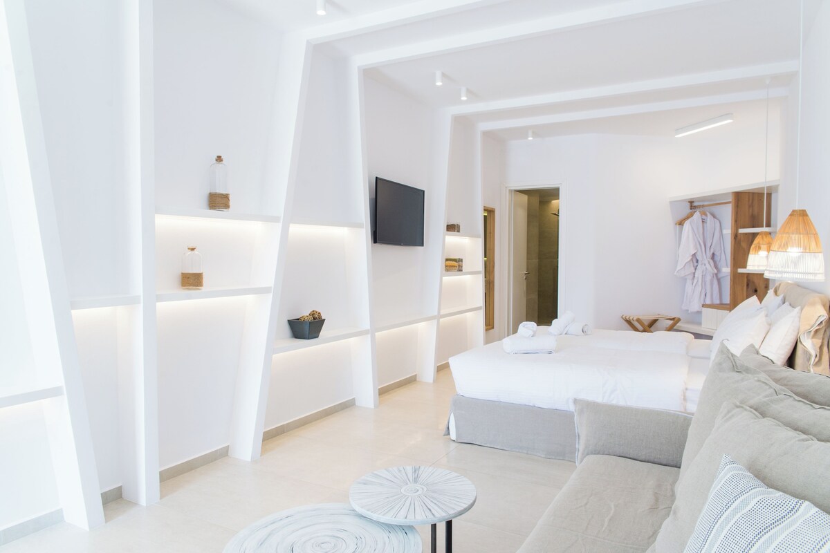 A modern hotel room with a large bed, a sofa, a small round table, and a TV mounted on the wall.