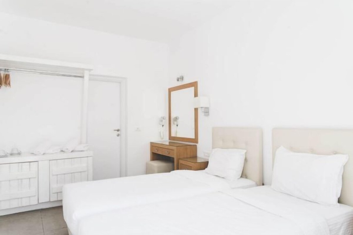 Una habitación de hotel con cama, tocador con espejo, armario blanco y una puerta.