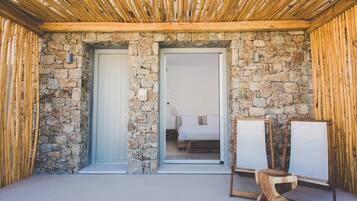 A room with stone walls, a wooden ceiling, and a bed with white linens. There are two easels with canvases leaning against the wall.