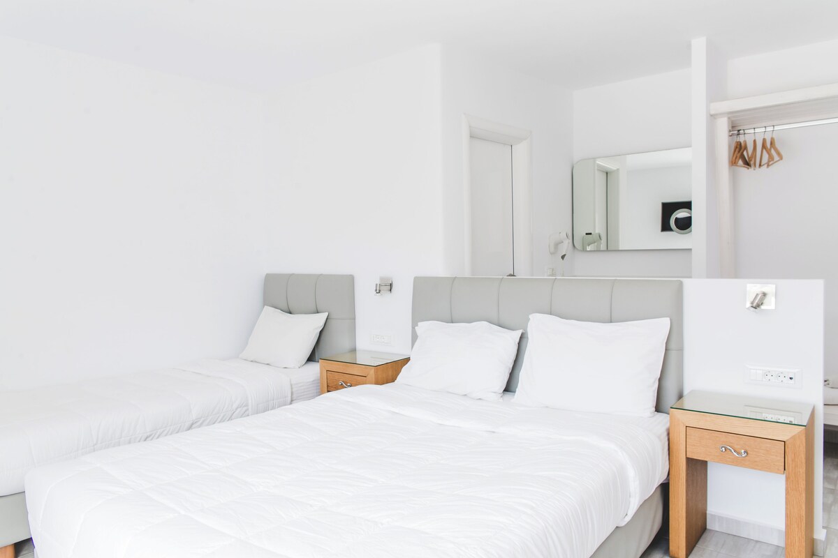 A hotel room with two beds, a mirror, a wardrobe, and a nightstand.