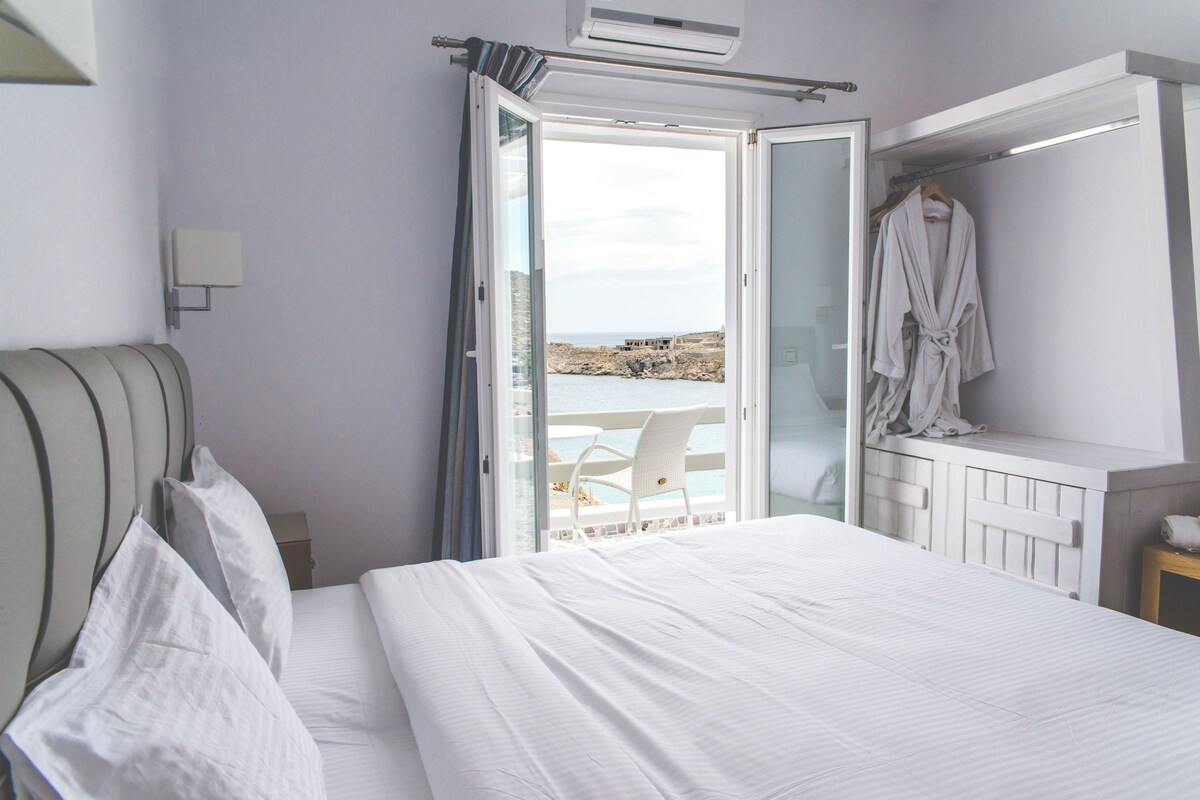 A bedroom with a bed, a chair by the window, and a robe hanging on a rack.