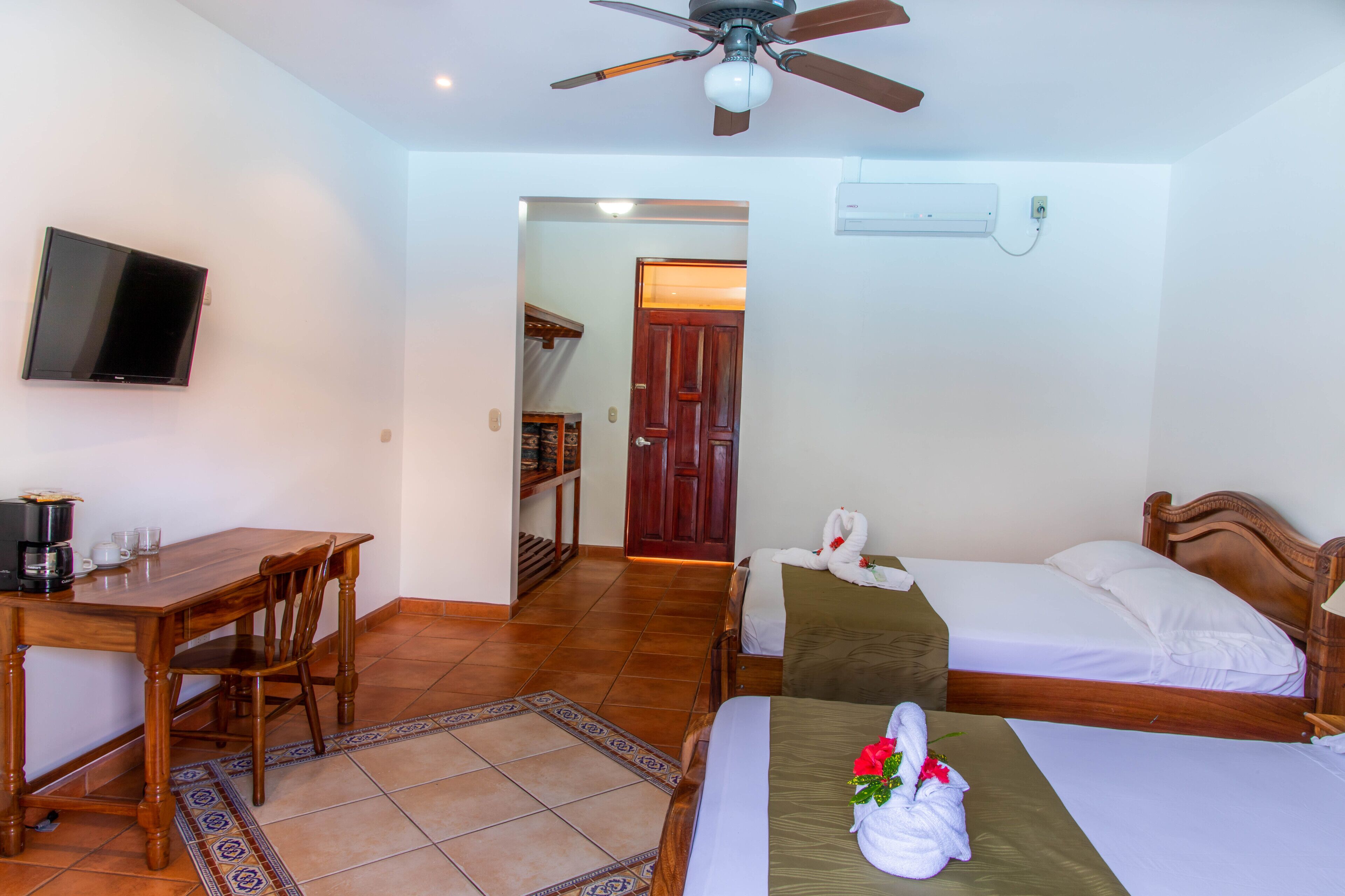 A hotel room with a bed, a desk, a chair, a television, and a ceiling fan.