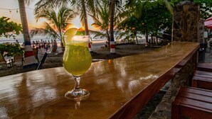 A bar with a glass of drink, palm trees, and a sunset in the background. - Hotel South Beach (Jacó)