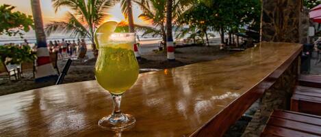 Un bar con una copa, palmeras y un atardecer de fondo.