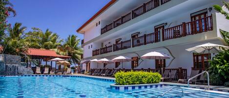 Un hotel con piscina, mobiliario exterior y un edificio de dos pisos con balcones.