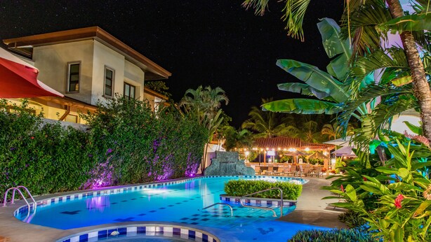 A swimming pool with a hot tub, surrounded by lush greenery and a building with a red awning. - Hotel South Beach (Jacó)