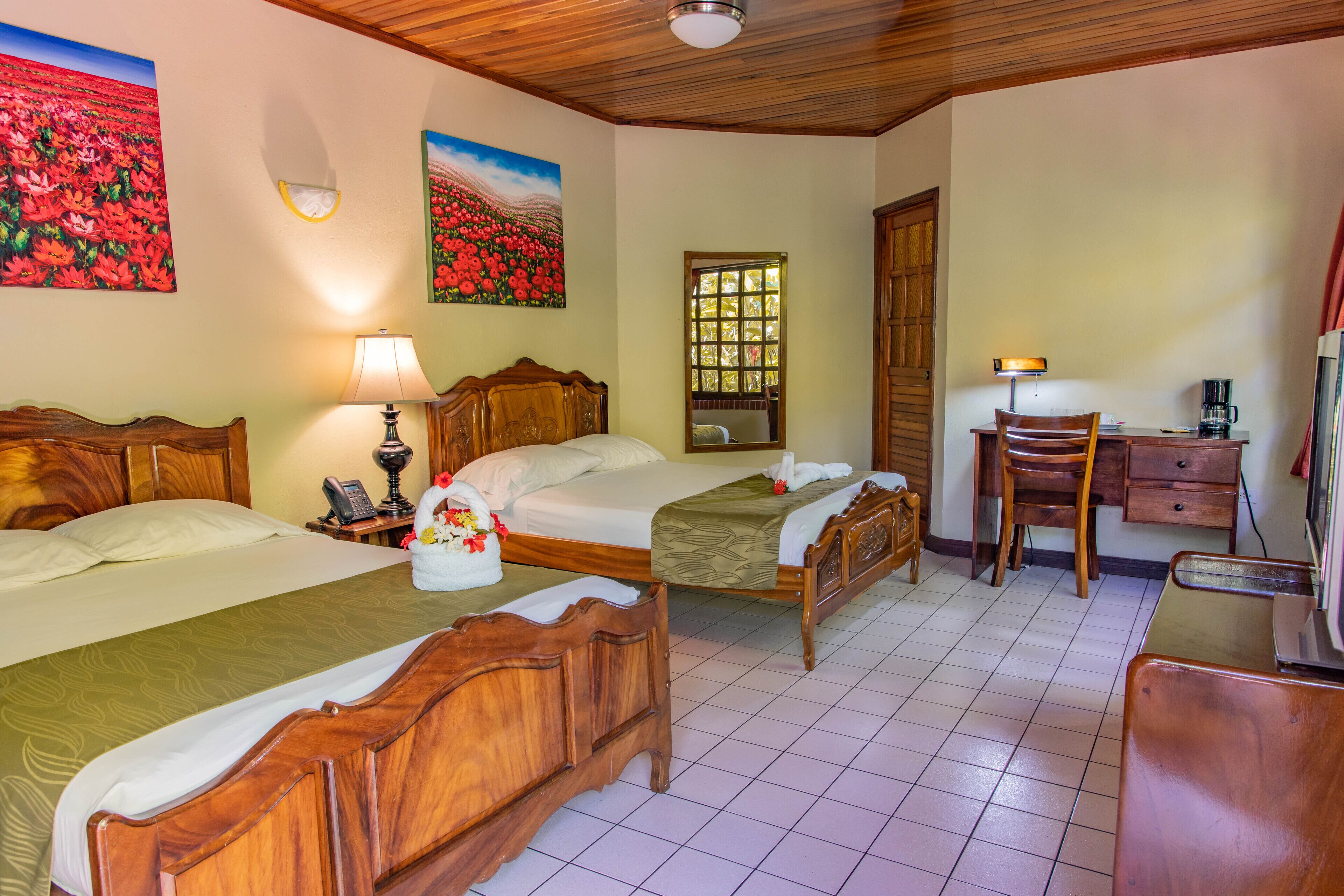 A hotel room with two wooden beds, a desk, a chair, a lamp, and a coffee maker.