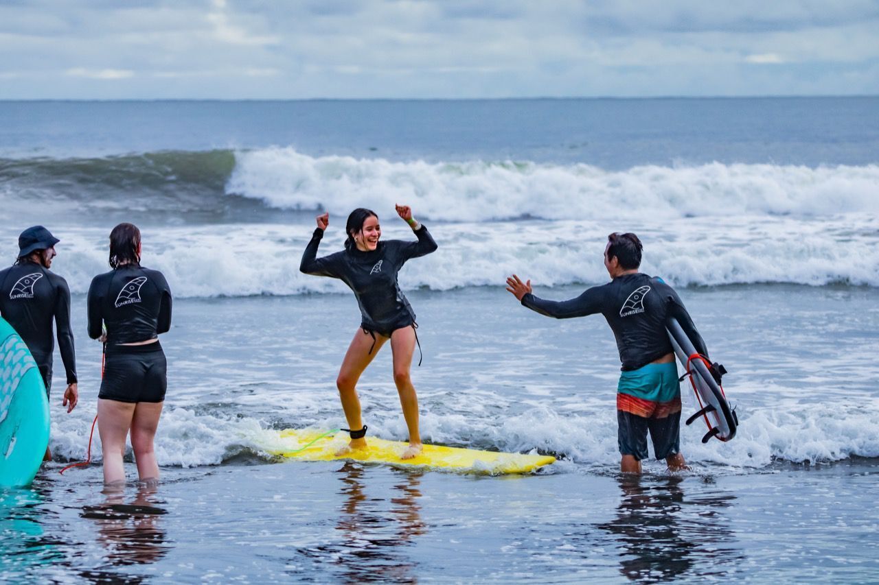 A group of people on a beach with surfboards, standing in shallow water.