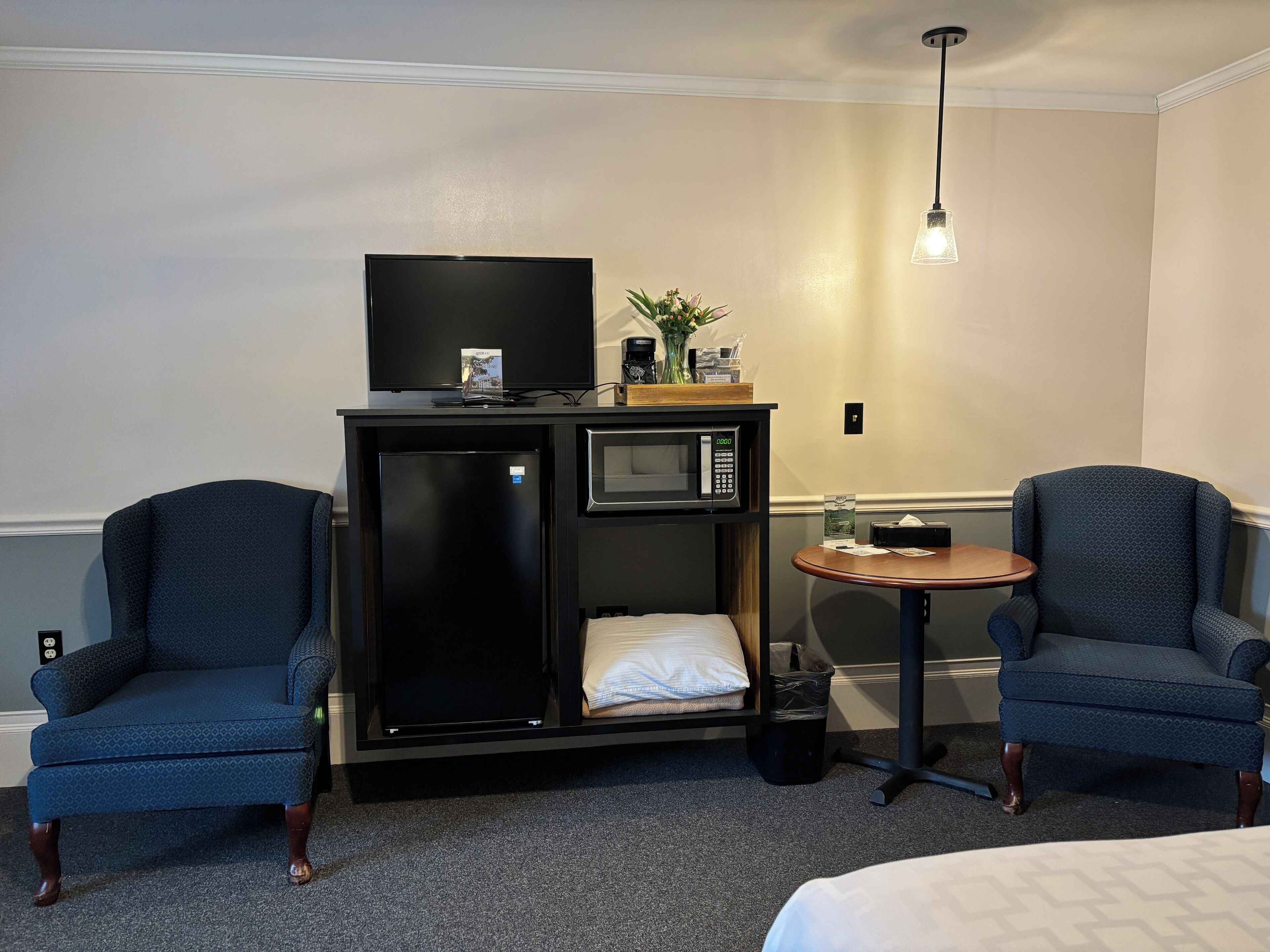 A compact hotel room with a bed, two armchairs, a small table, a minibar, a television, and a microwave.