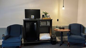A compact hotel room with a bed, two armchairs, a small table, a minibar, a television, and a microwave.