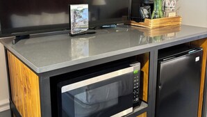 Una kitchenette compacta con microondas integrado, un refrigerador pequeño y un televisor de pantalla plana.