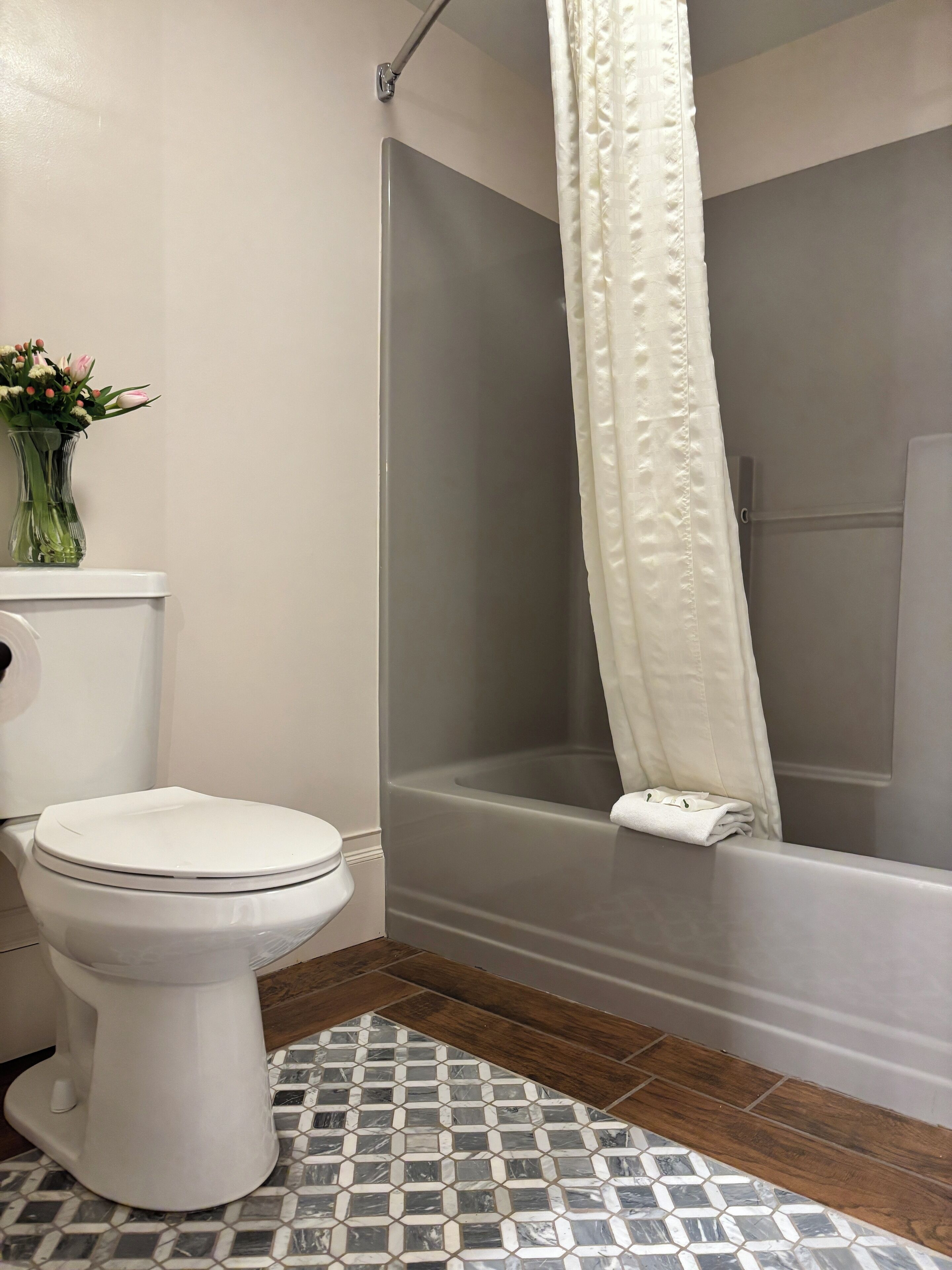 A bathroom with a toilet, a shower with a white curtain, and a tiled floor.