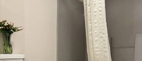 A bathroom with a toilet, a shower with a white curtain, and a tiled floor.