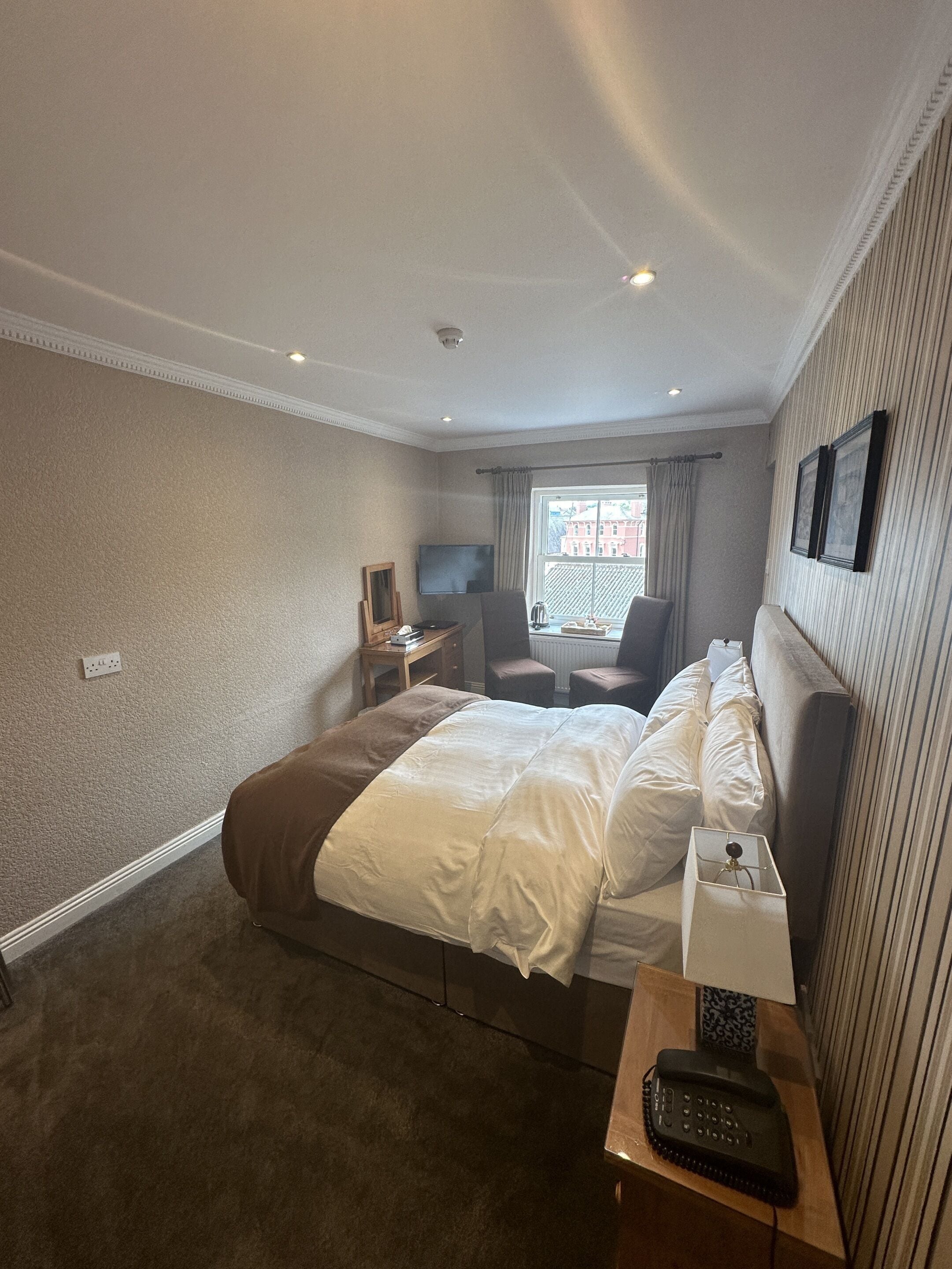 A hotel room with a large bed, a desk with a lamp, a chair, a television, and a window with curtains.