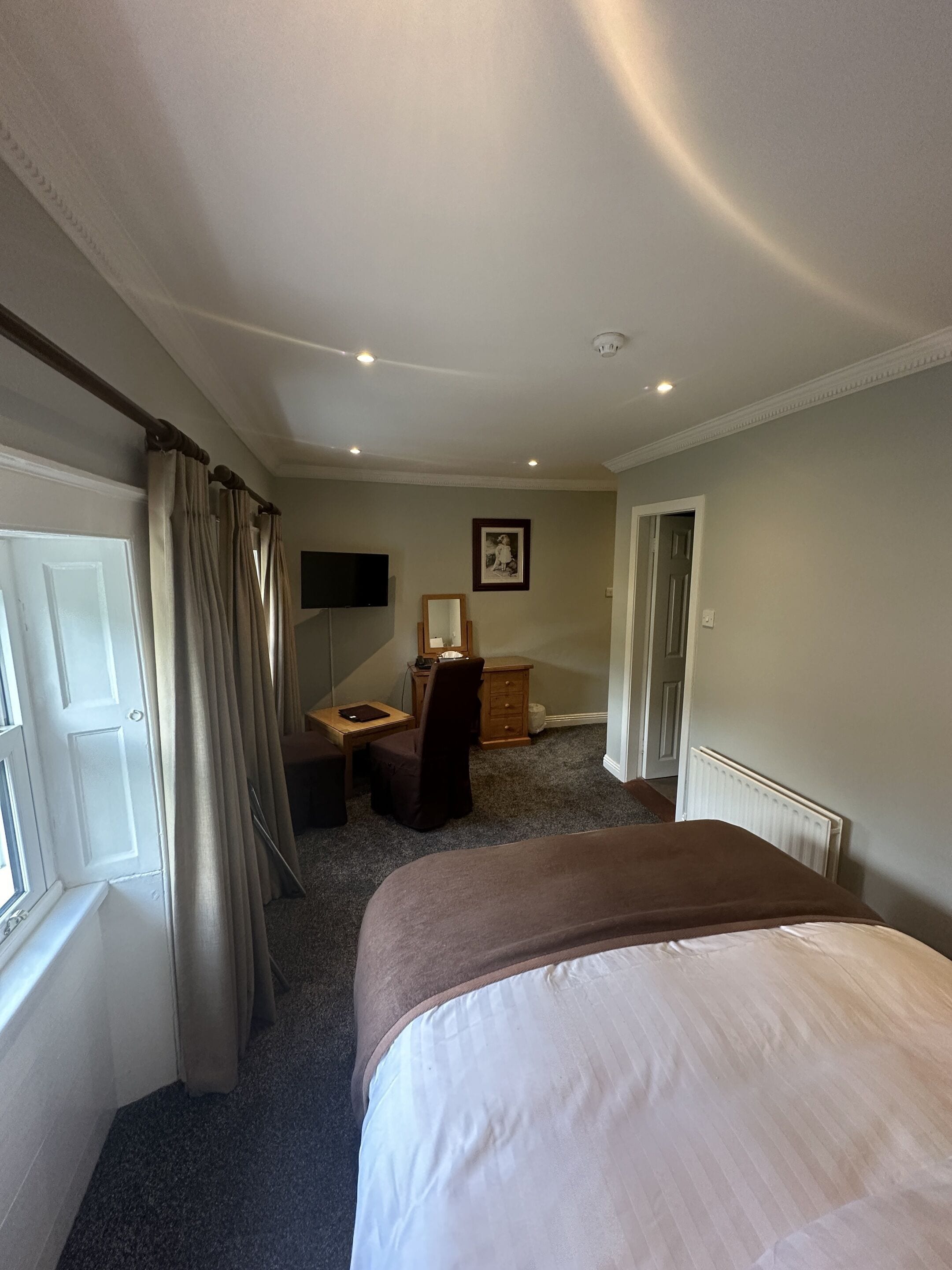 Una habitación de hotel con cama, escritorio, silla, televisor y un cuadro en la pared.