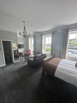 A hotel room with a large bed, a sofa, a chair, a TV, and a view of the outside. - Long Quay House (Kinsale)