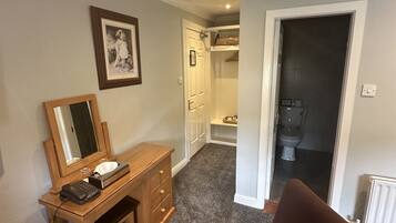 Une pièce avec un bureau en bois, une chaise, un miroir et un tableau encadré au mur. Une porte donne accès à une salle de bain.