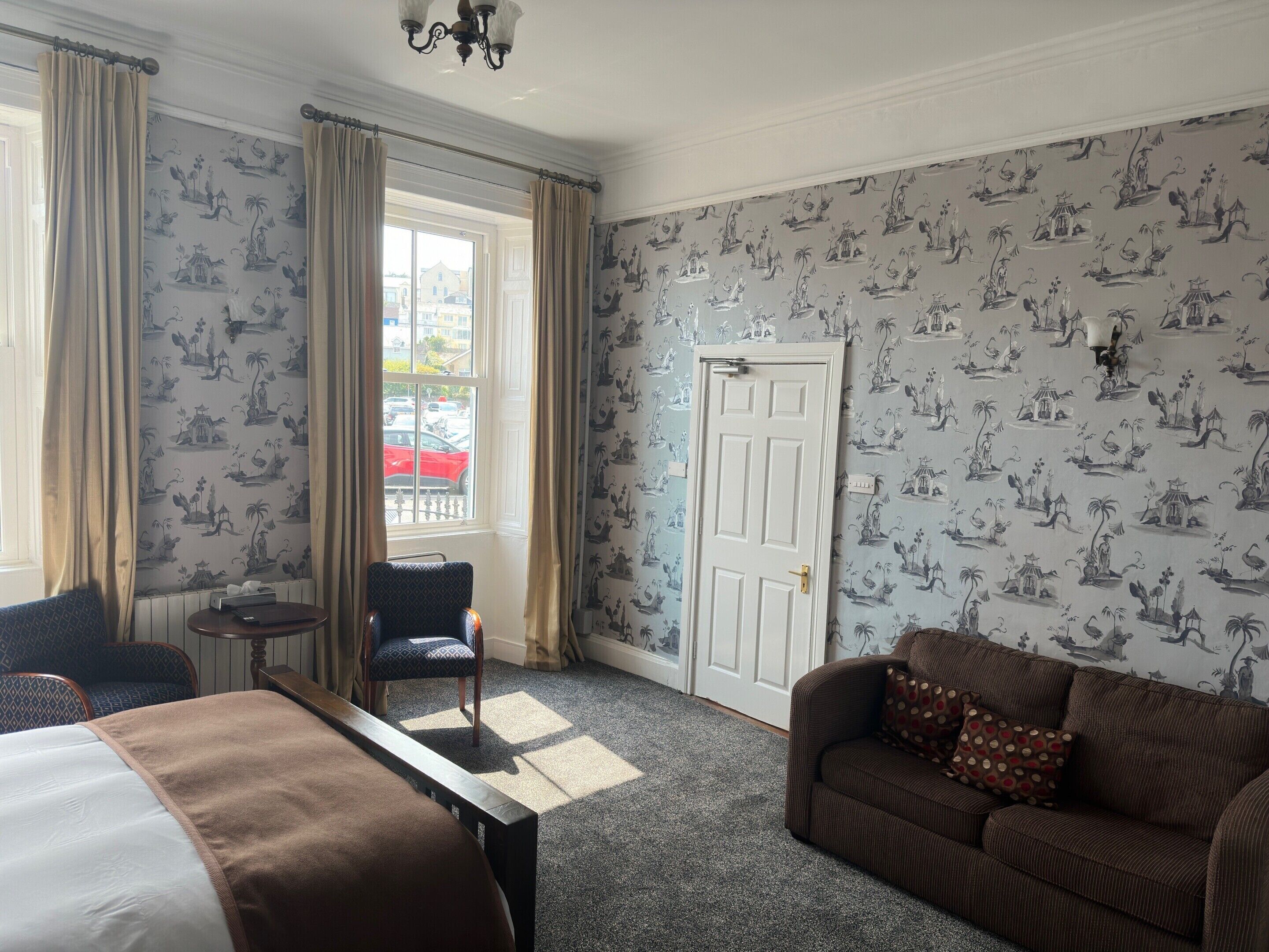 A hotel room with a bed, a sofa, a chair, a small table, and a window with curtains.