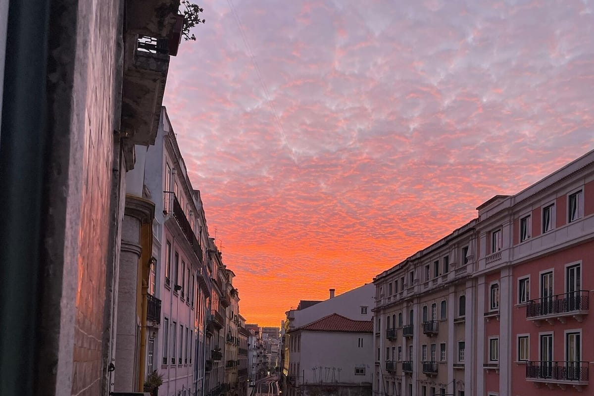 A street view at sunset with buildings on either side, a tram line, and parked cars.
