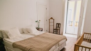 A bedroom with a bed, a chair, a small table with a lamp, and a window. - Asul B&B (Lisbon)