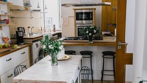A compact kitchen with a central island, a washing machine, and a dining area with chairs. - Asul B&B (Lisbon)
