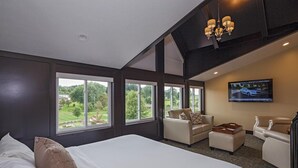A modern hotel room with a large bed, two sofas, a TV, and large windows offering a view of the outdoors. - Berlin Resort (Millersburg)