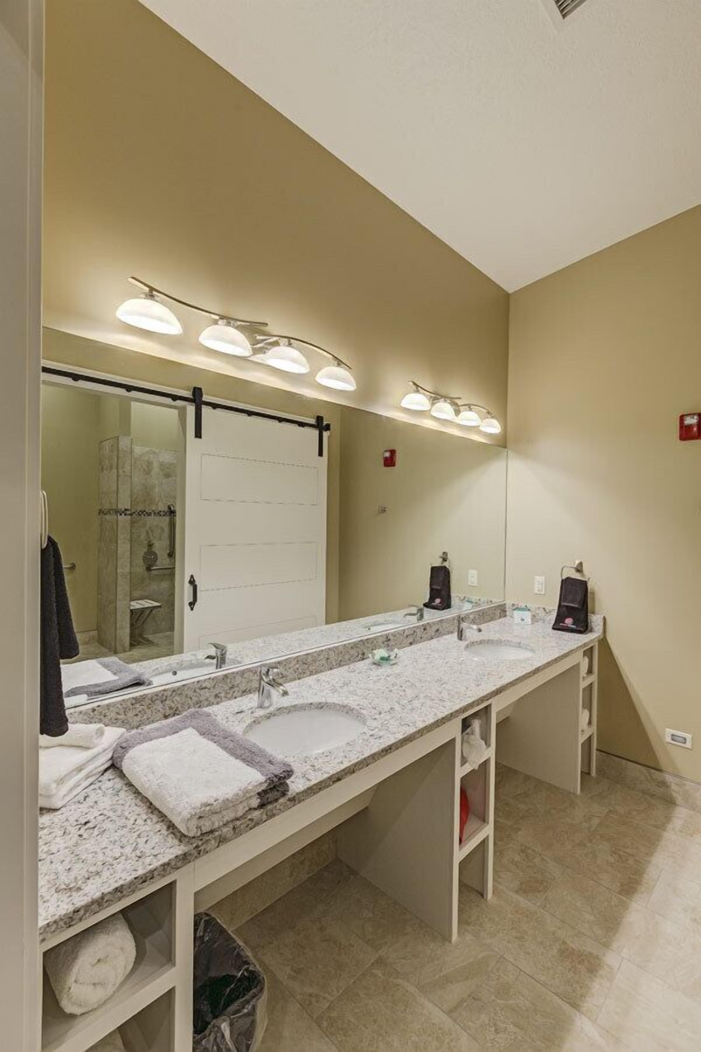 A bathroom with a large mirror, two sinks, a towel rack, and a shower area.
