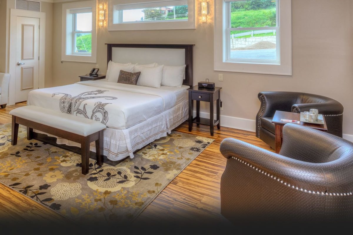 A bedroom with a large bed, a bench, a chair, and a small table.