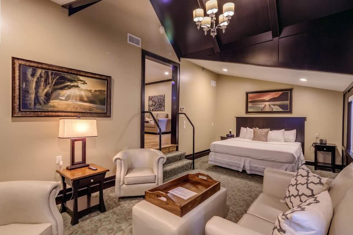 A hotel room with a large bed, a sofa, a chair, a desk, and a chandelier.