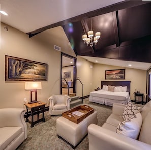 A hotel room with a large bed, a sofa, a chair, a desk, and a chandelier.