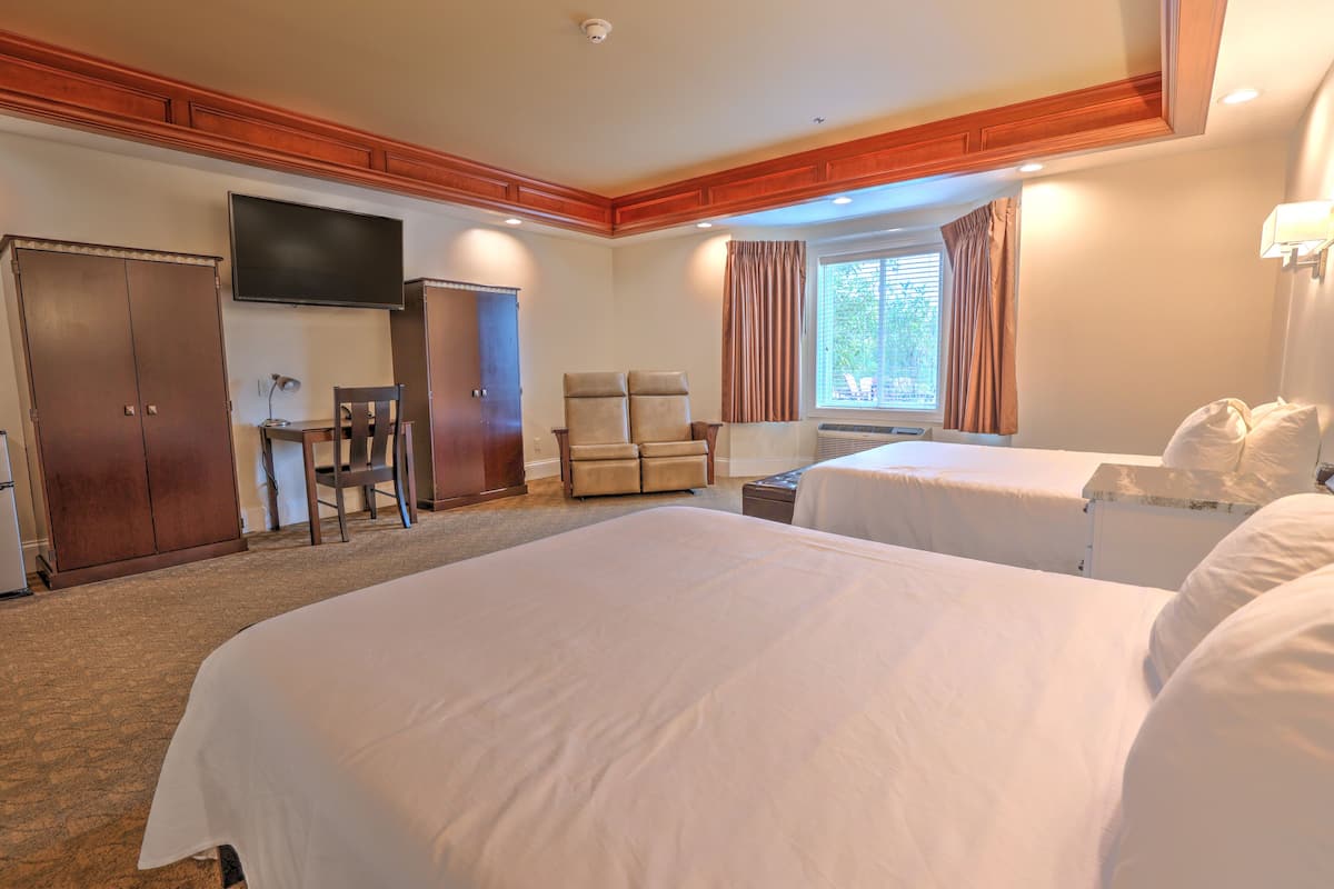 A hotel room with two beds, a TV, a desk, a chair, and a wardrobe.