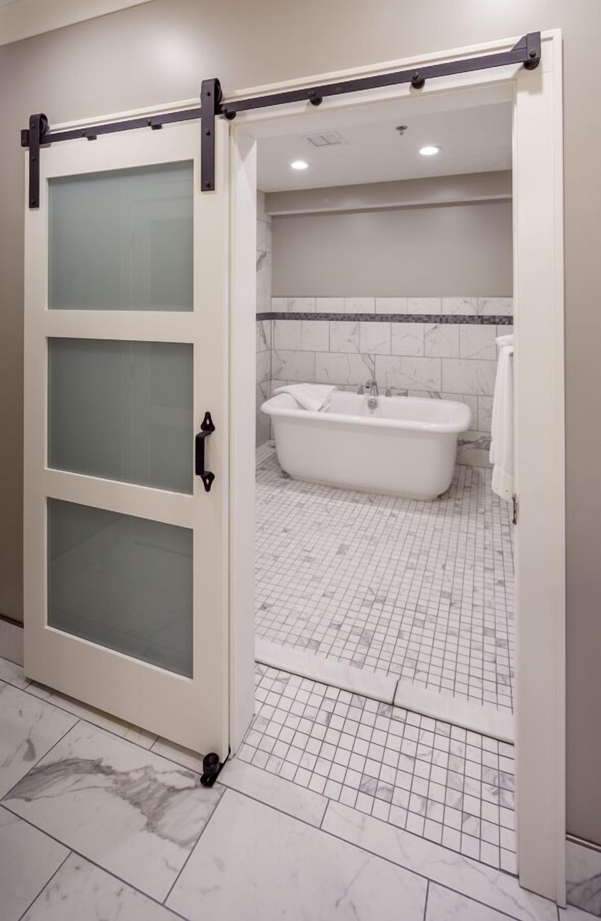 Une salle de bain avec une baignoire blanche, un carrelage au sol et une porte coulissante en verre dépoli.