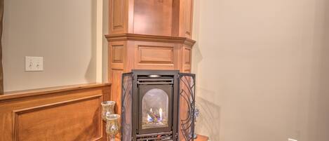 Una chimenea en esquina con repisa, puerta de cristal y un pequeño estante con adornos.