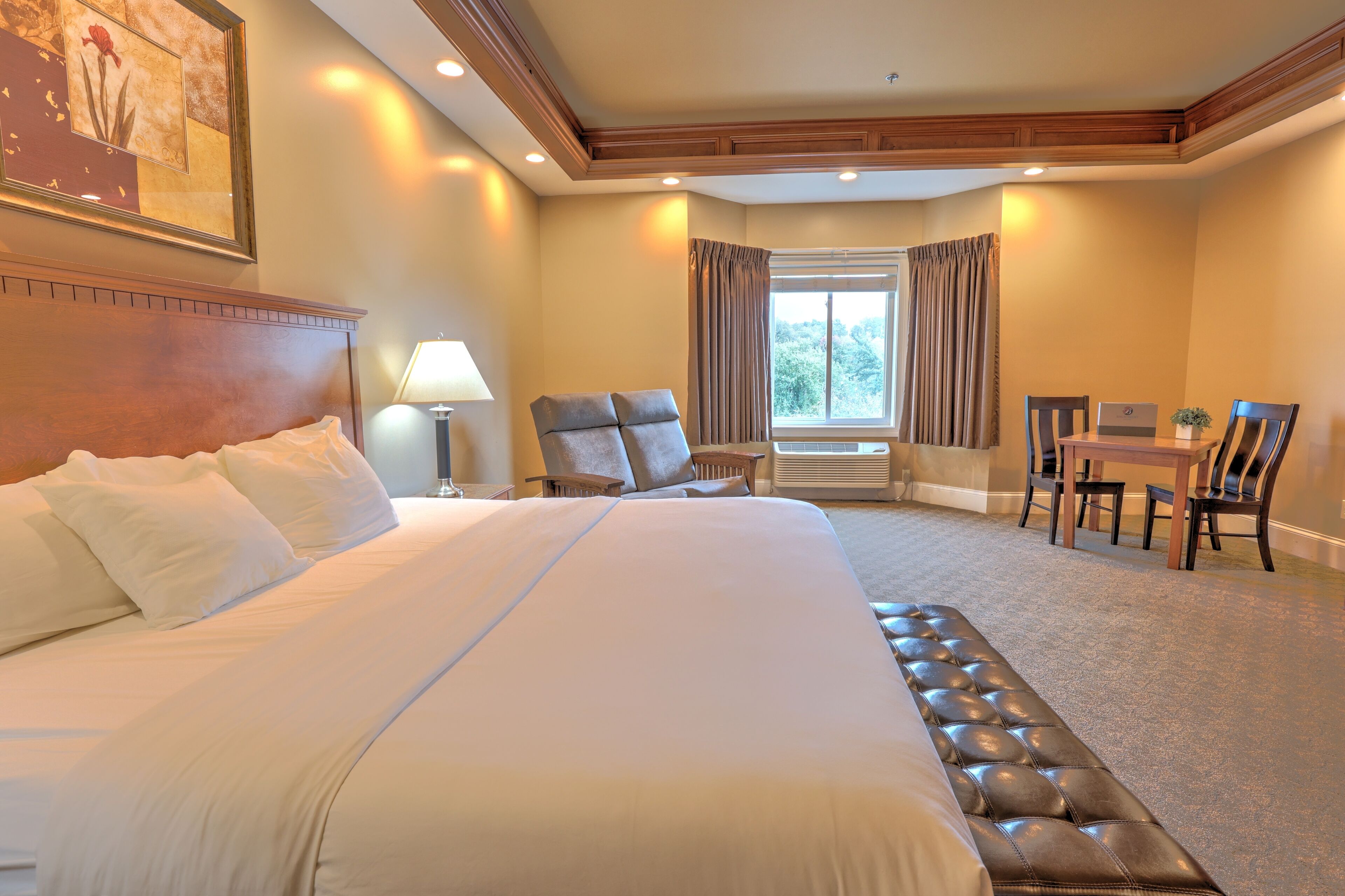 Una habitación de hotel con una cama grande, un escritorio con dos sillas, una ventana con cortinas y un cuadro en la pared.