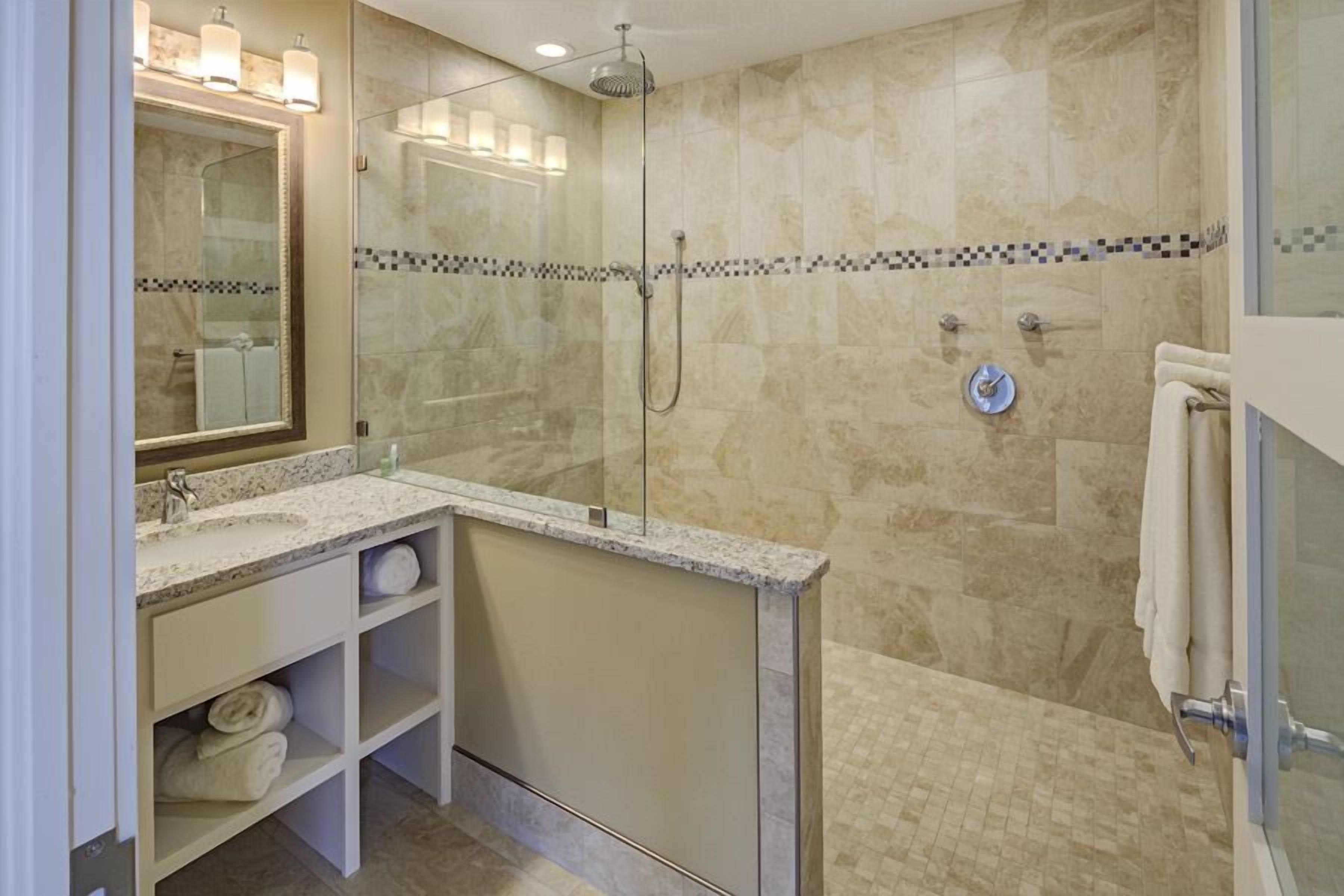 Un baño moderno con ducha de vidrio, un espejo grande y encimera de mármol.