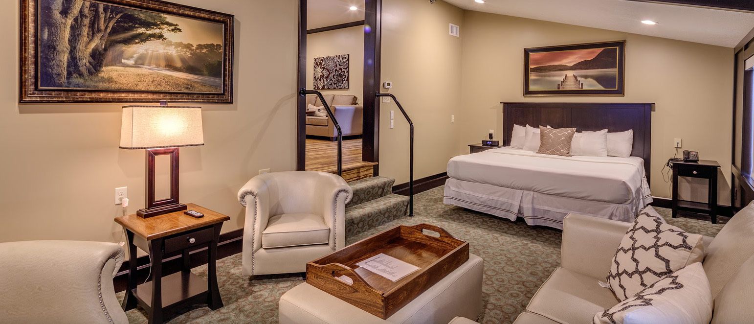 A hotel room with a large bed, a desk with a lamp, a chair, and a wooden tray.