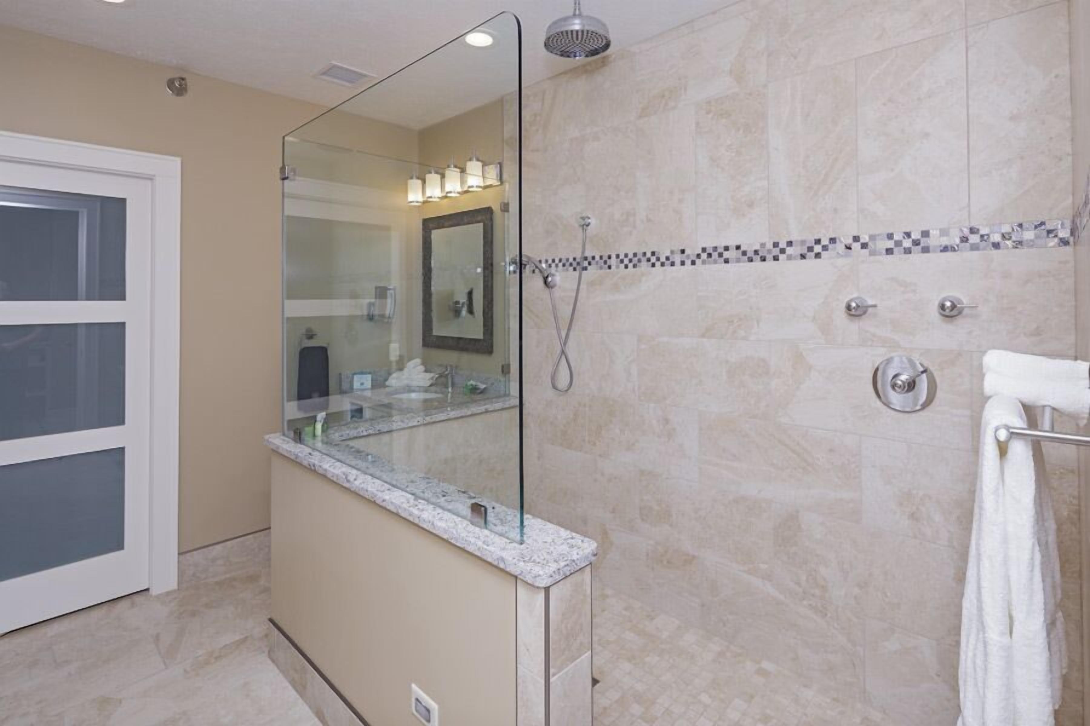 Un baño moderno con cabina de ducha de vidrio, tocador con espejo y pared de ducha con azulejos.