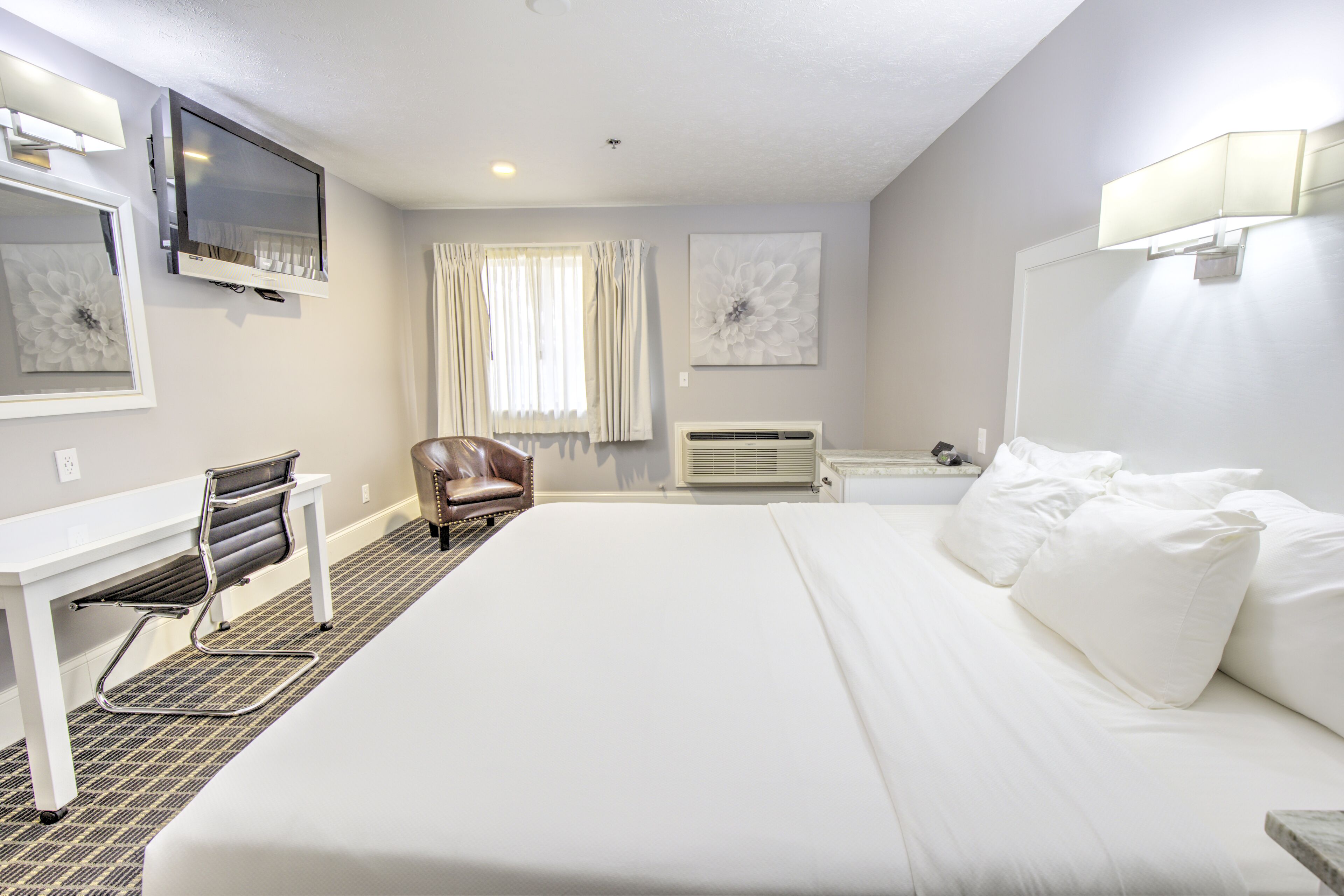 A hotel room with a large bed, a desk with a chair, a television, and a window with curtains.