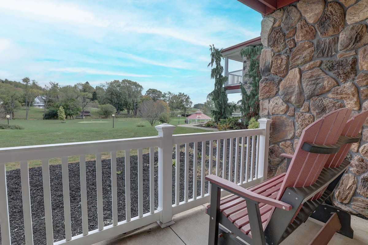 A stone exterior wall, a white railing, and a red Adirondack chair.
