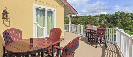 A deck with wooden chairs and a table, a white railing, and a building with a door and window.