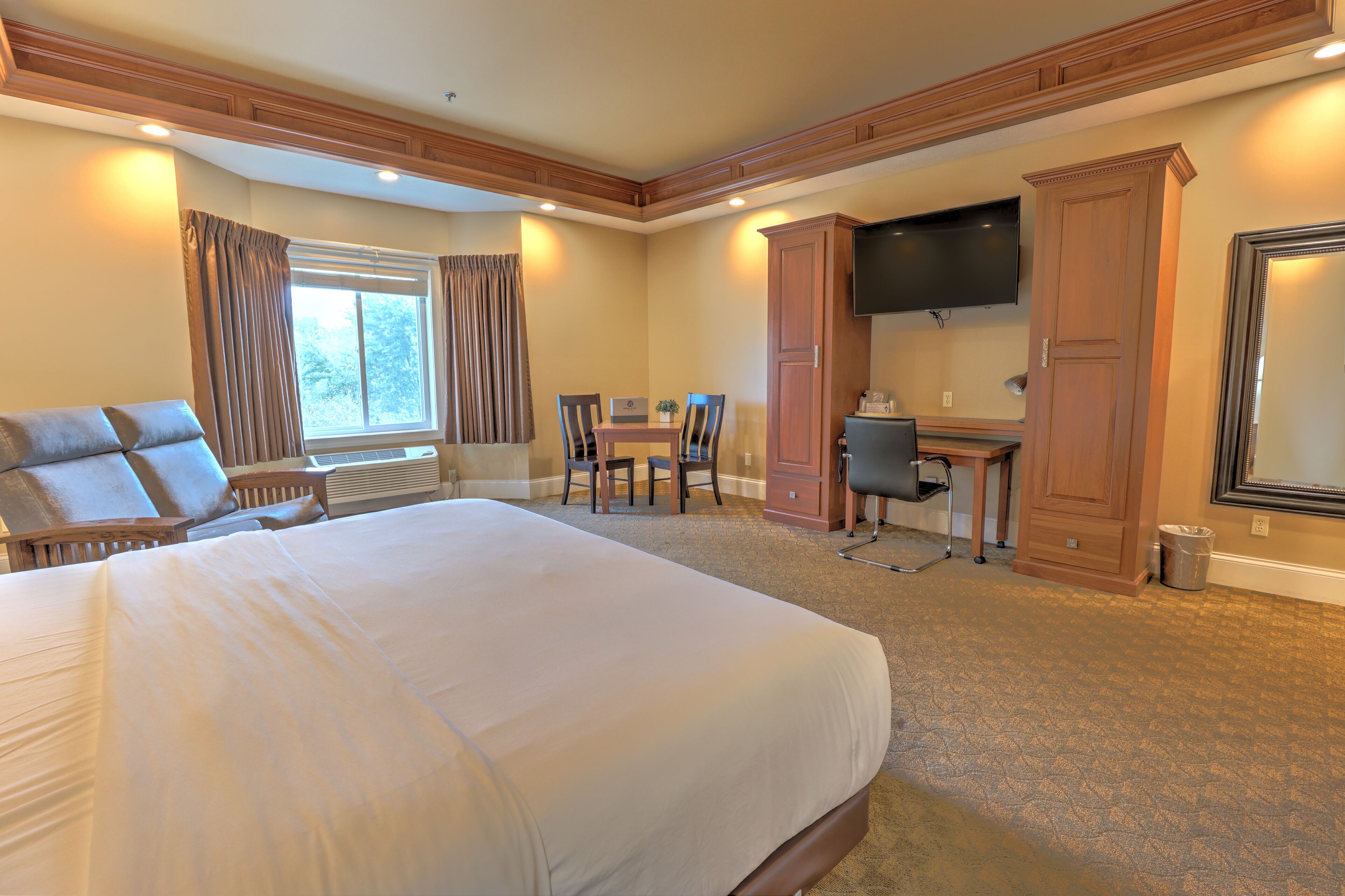 A hotel room with a large bed, a desk, a chair, a television, and a wardrobe.