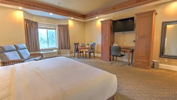A hotel room with a large bed, a desk, a chair, a television, and a wardrobe.