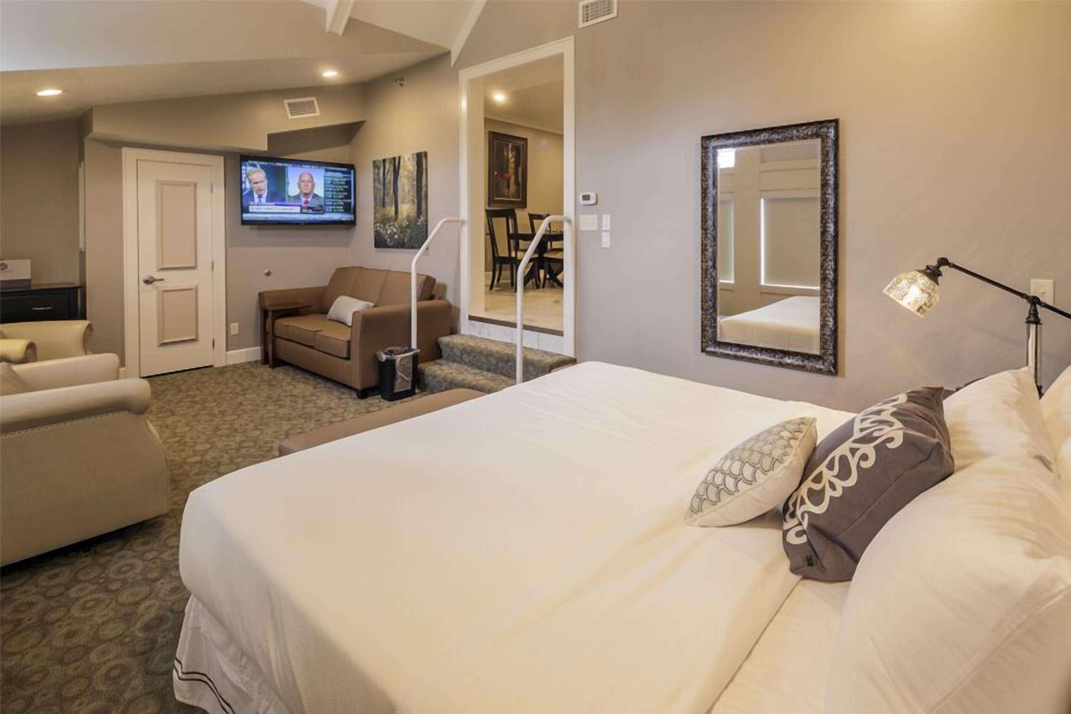 Una habitación de hotel con cama, sofá, televisión, espejo y lámpara.