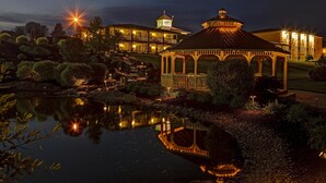 A well-lit gazebo with a reflection in a pond, surrounded by landscaped gardens and a large building with multiple balconies and a tower. - Berlin Resort (Millersburg)