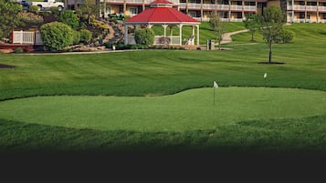 A golf course with a gazebo, a well-maintained lawn, and a building with multiple balconies in the background.