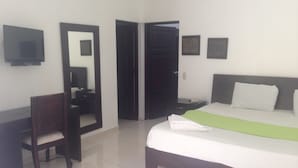 A hotel room with a bed, a desk, a chair, a mirror, and a wardrobe. - Sosua Sunset Hotel (Sosúa)