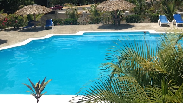 A swimming pool with lounge chairs and thatched umbrellas, surrounded by lush greenery. - Sosua Sunset Hotel (Sosúa)