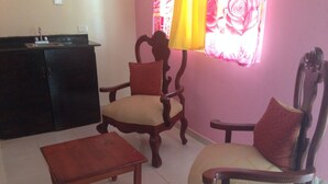 A living room with two wooden chairs, a small wooden table, and a kitchen area with a sink. - Sosua Sunset Hotel (Sosúa)