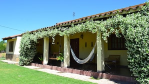 Una casa con porche, cubierta de plantas trepadoras, y una hamaca.
