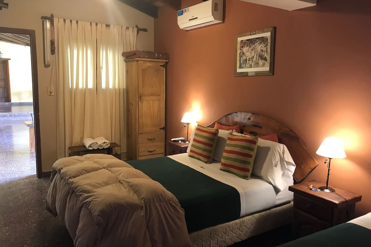A hotel room with a wooden bed, a wooden wardrobe, a bedside table with a lamp, and a picture on the wall.